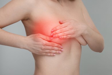 Naked young woman suffering from breast pain on light grey background, closeup