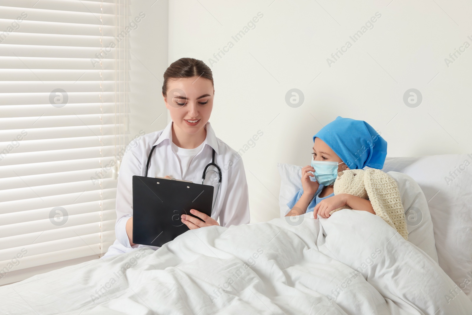 Photo of Childhood cancer. Doctor with clipboard and little patient with toy bunny in hospital