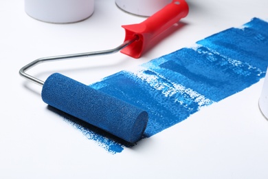 Roller brush with blue paint near cans on white background