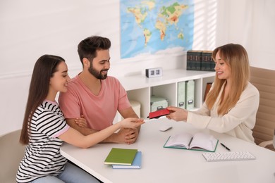 Photo of Manager giving passports to couple at desk in travel agency