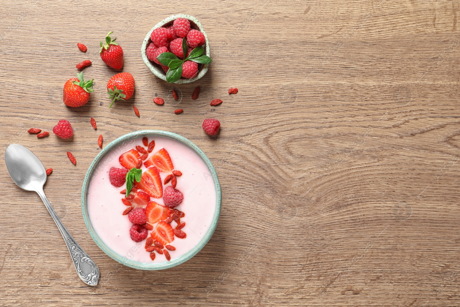 Photo of Smoothie bowl with goji berries and spoon on wooden table, flat lay. Space for text