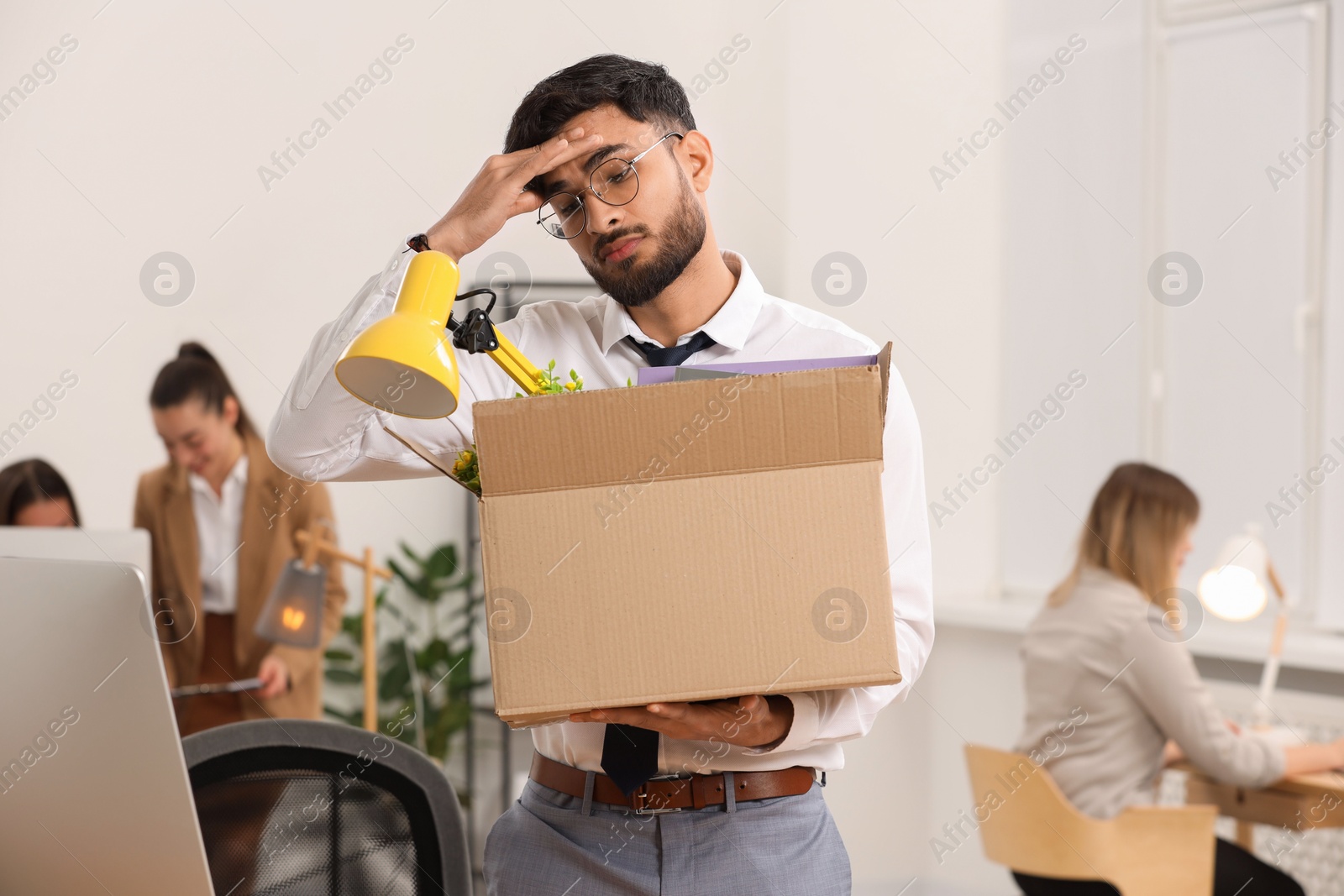 Photo of Unemployment problem. Frustrated man with box of personal belongings in office