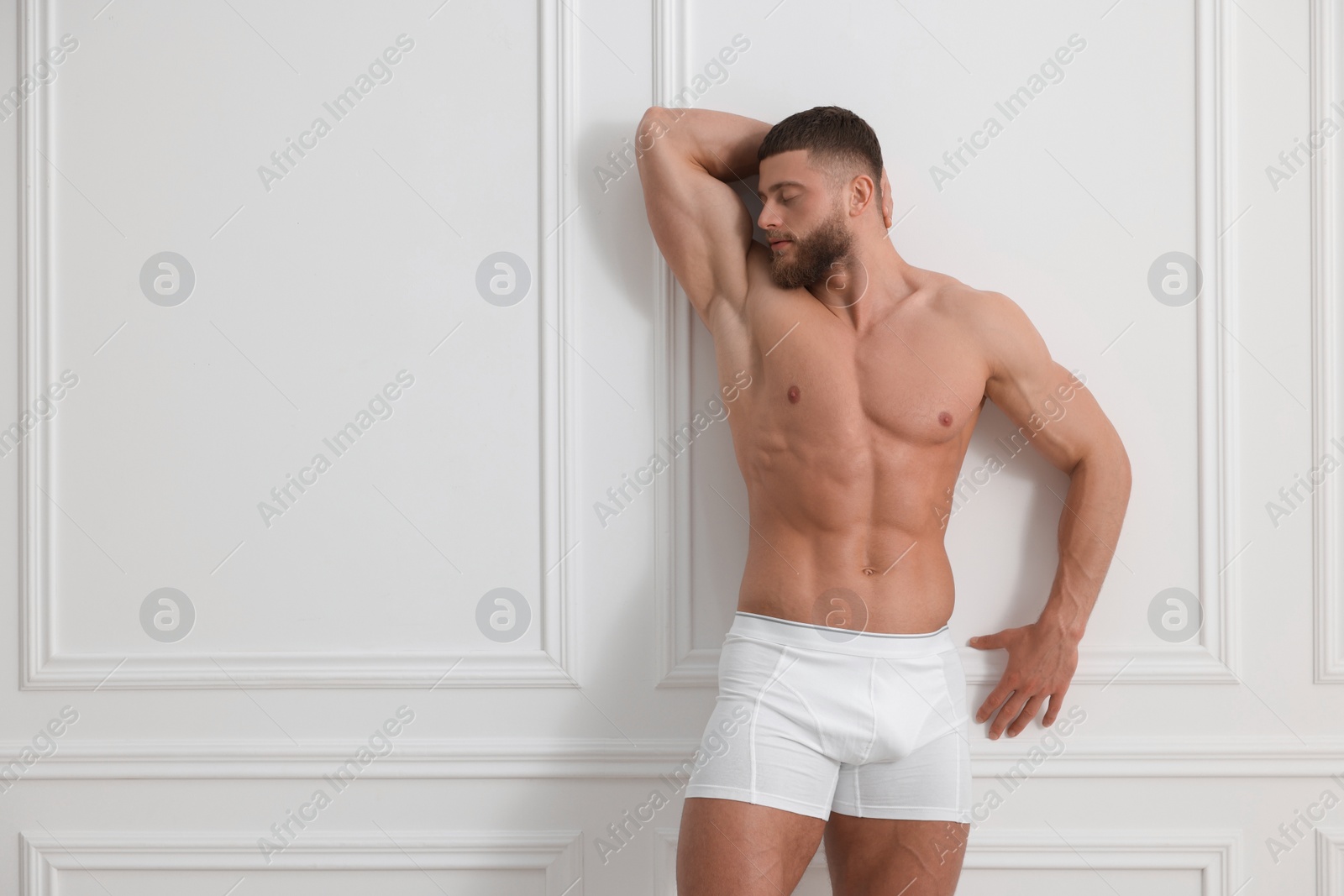 Photo of Young man in stylish underwear near white wall indoors. Space for text