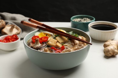 Photo of Bowl of delicious ramen, ingredients and chopsticks on white table, closeup. Noodle soup