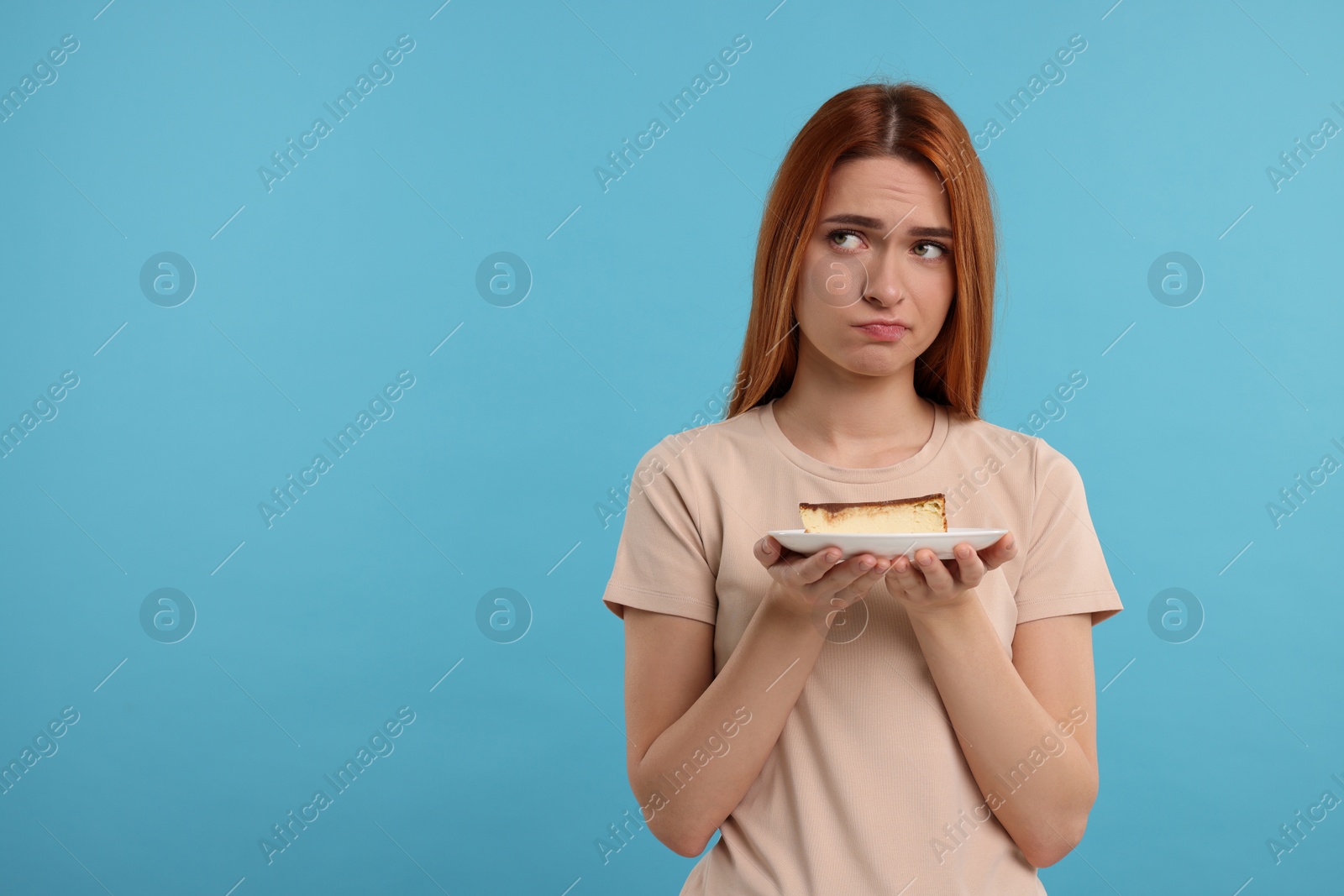 Photo of Unhappy young woman with piece of tasty cake on light blue background, space for text