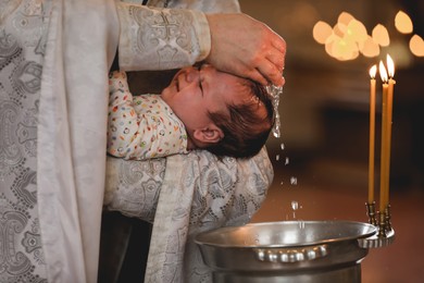 Photo of Priest baptizing adorable baby in church, closeup