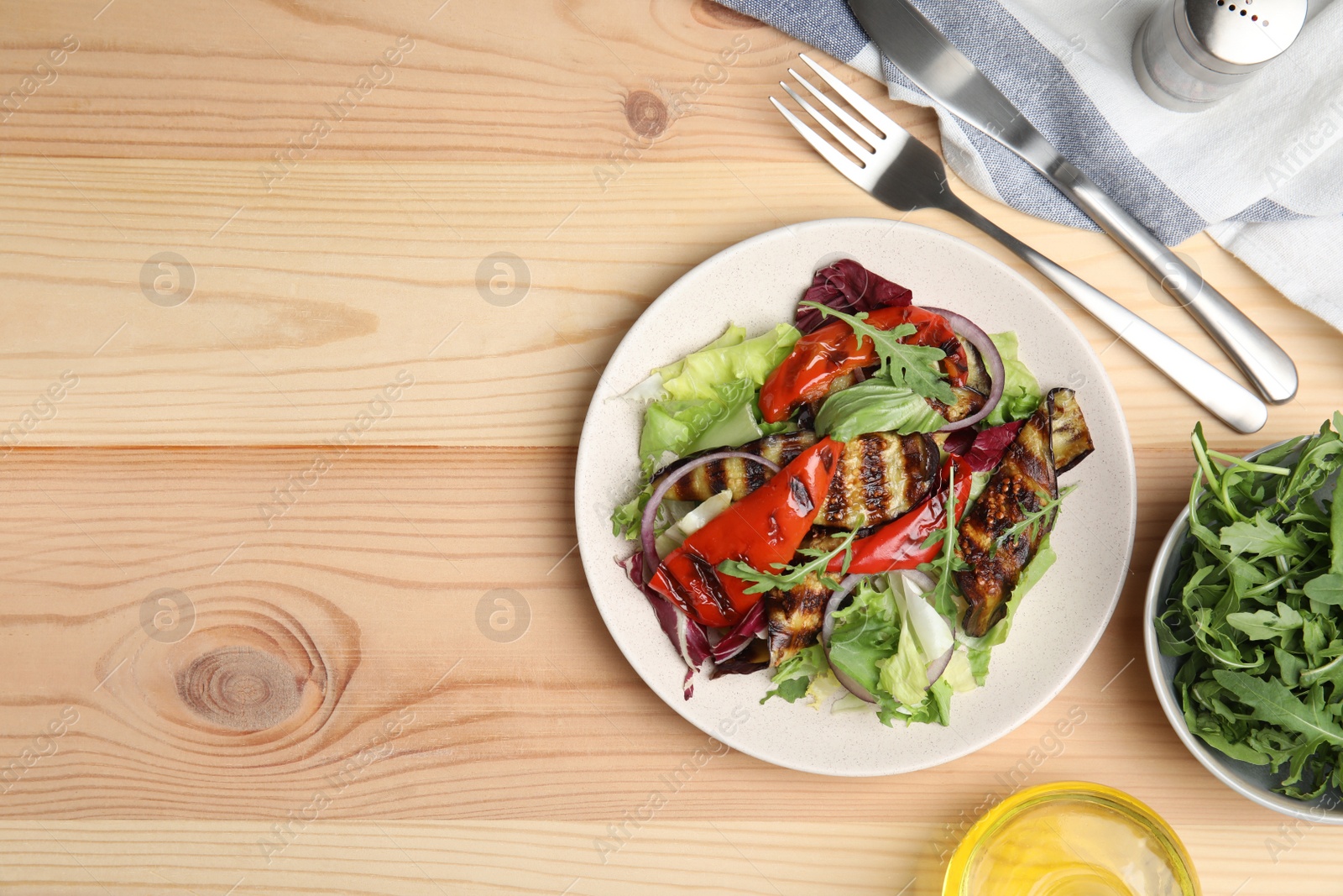 Photo of Delicious salad with roasted eggplant and arugula served on wooden table, flat lay. Space for text