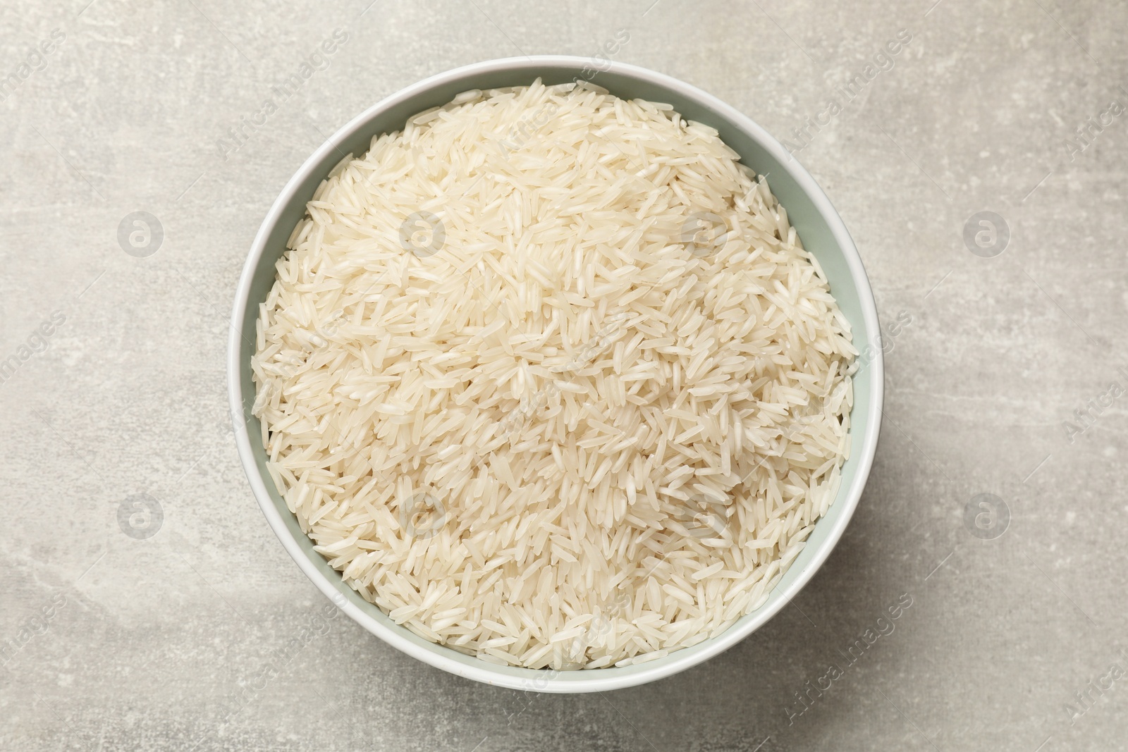 Photo of Raw basmati rice in bowl on grey table, top view