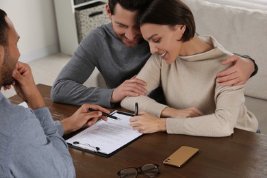 Photo of Professional notary helping couple with paperwork at wooden table