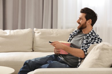 Photo of Happy man watching TV with popcorn on sofa indoors