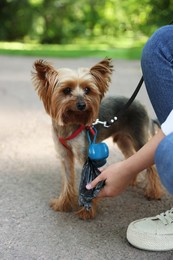 Photo of Woman with cute dog taking waste bag from holder in park, closeup