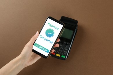Image of Woman using terminal for contactless payment with smartphone on brown background, top view. Transaction completed screen on device