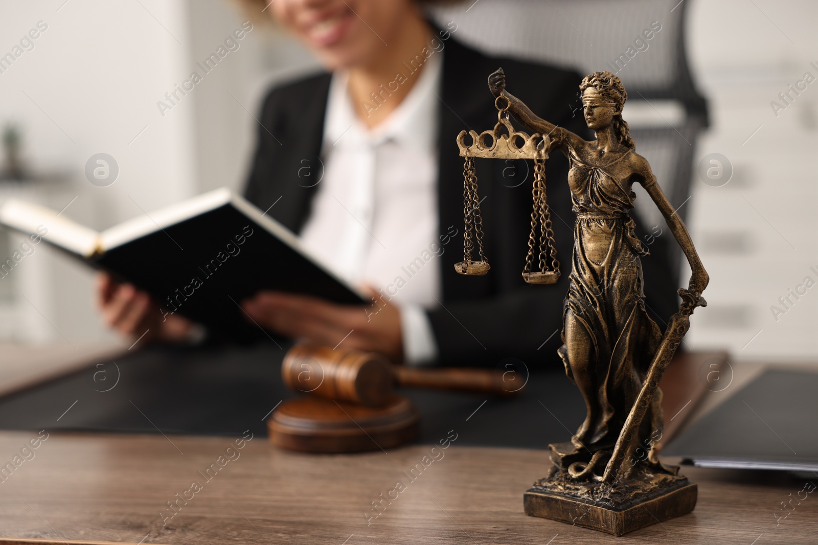 Photo of Notary with notebook at workplace in office, focus on statue of Lady Justice