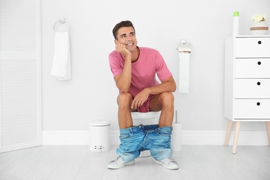 Young man sitting on toilet bowl at home