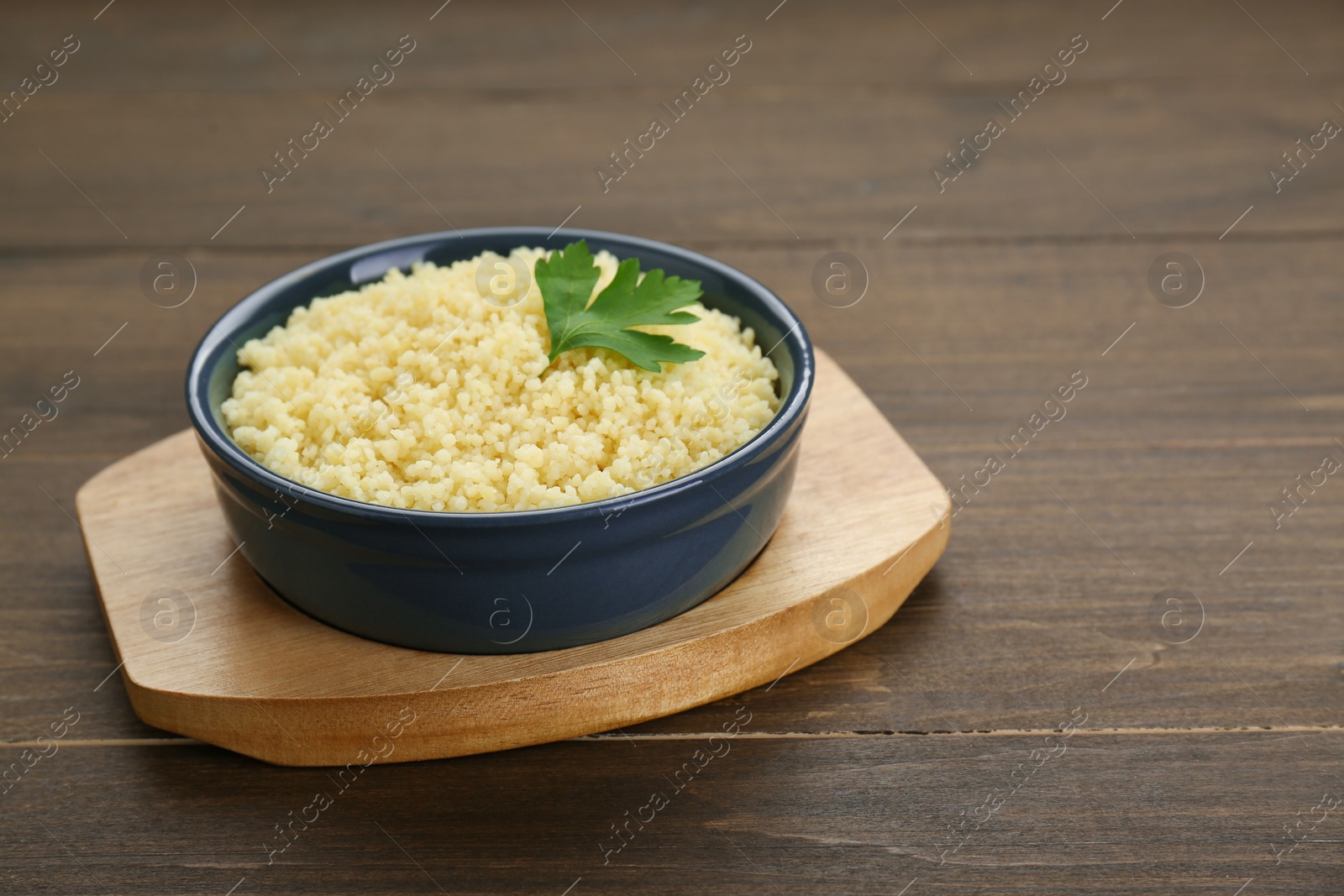 Photo of Tasty couscous with parsley on wooden table. Space for text