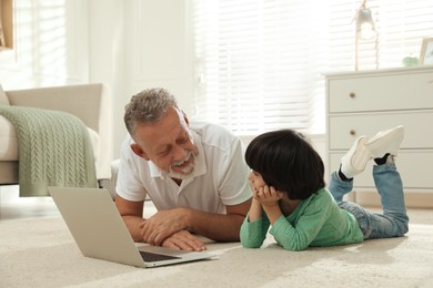 Photo of Grandfather and his grandson using laptop together on floor at home