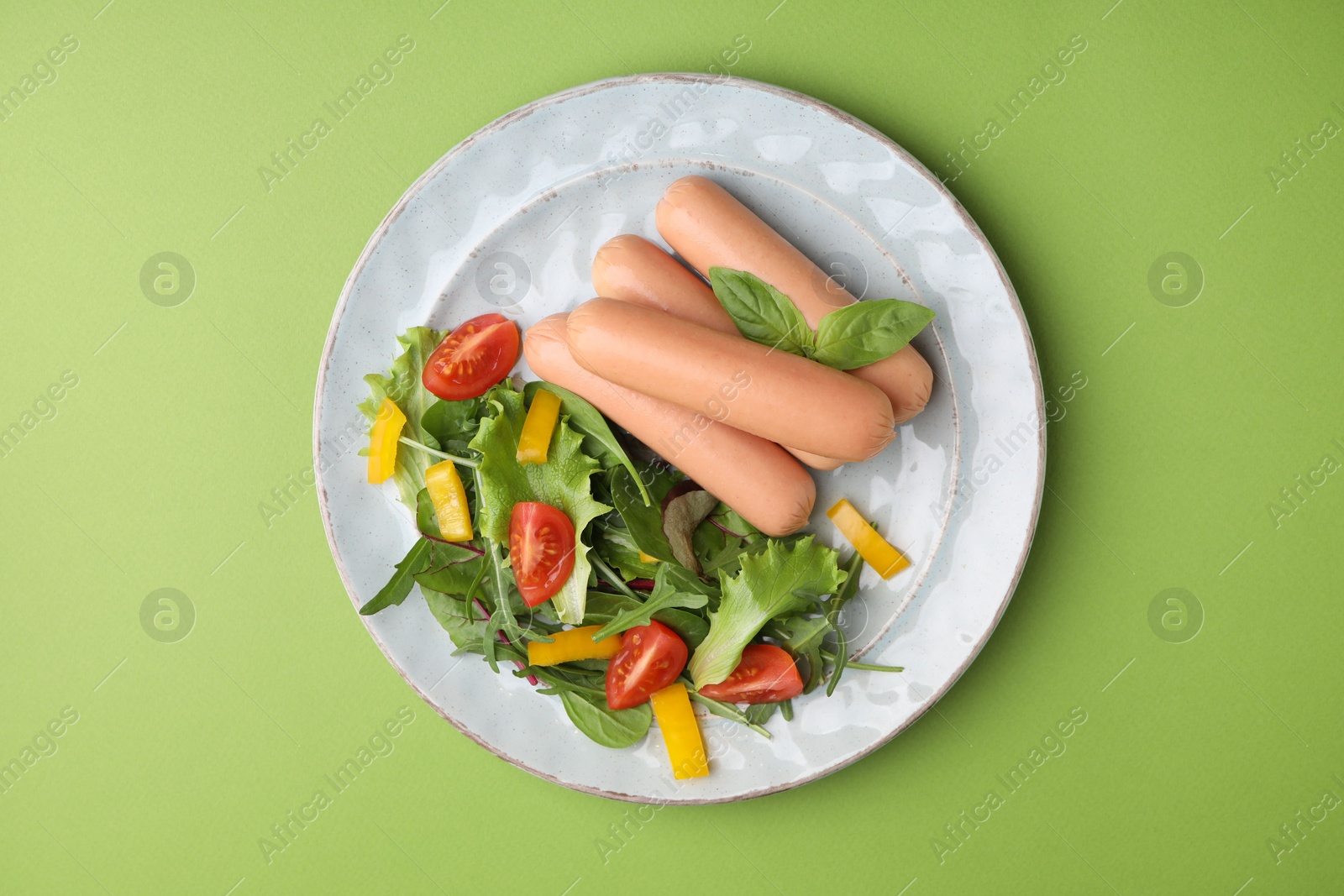 Photo of Delicious boiled sausages with salad on green, top view