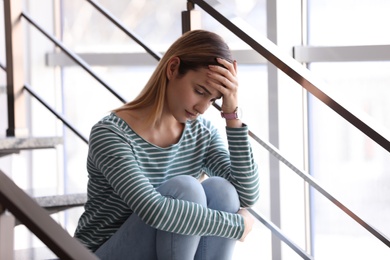 Photo of Emotional teenage girl sitting on stairs indoors