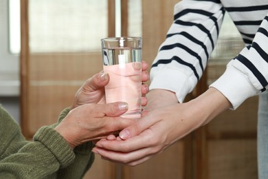 Caregiver giving water to elderly woman at home, closeup