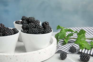 Photo of Tray with bowls of tasty blackberries on grey marble table against blue background