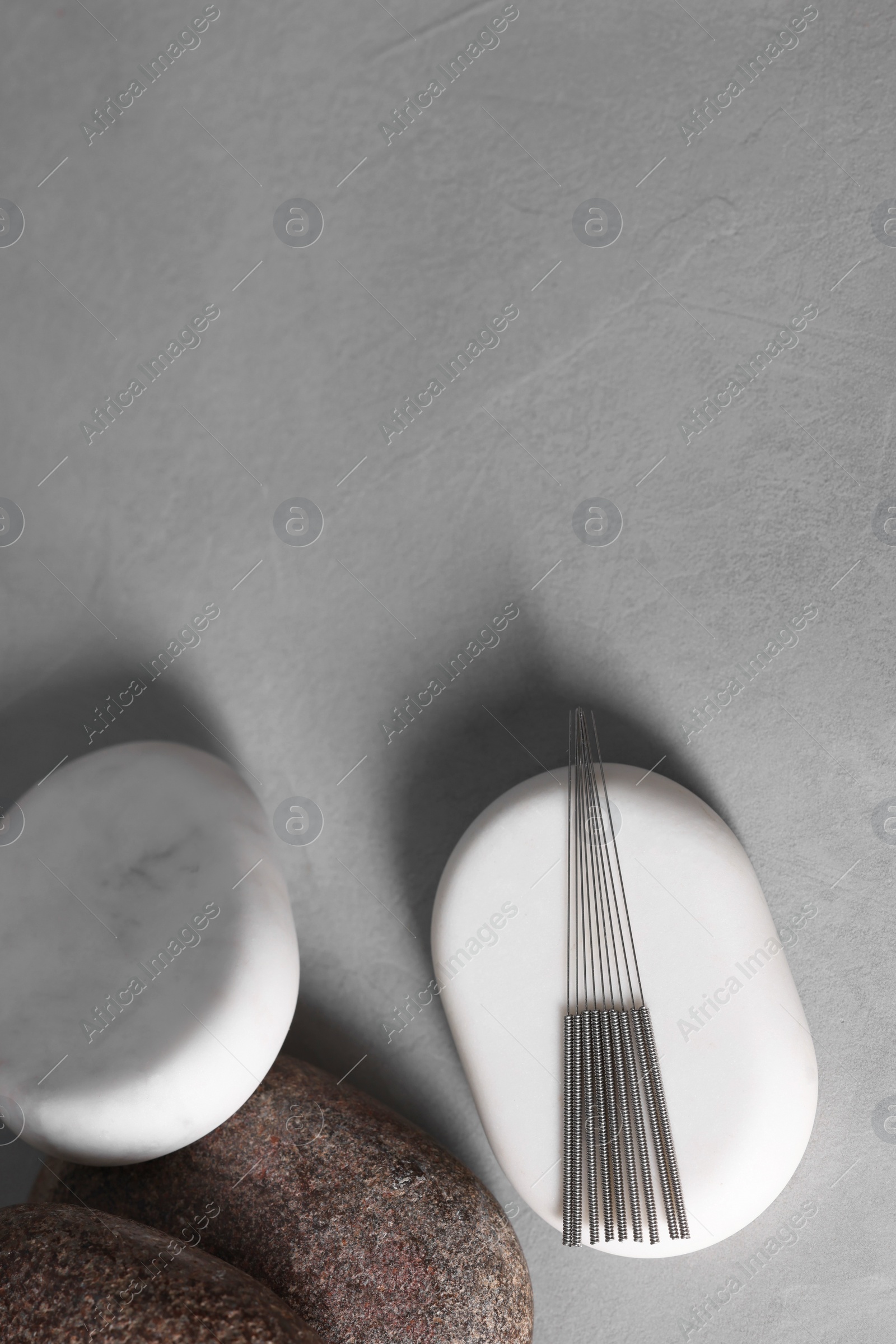 Photo of Stones with acupuncture needles on grey table, flat lay. Space for text