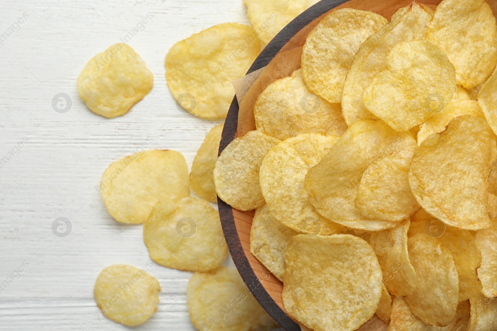 Photo of Delicious crispy potato chips in bowl on table, top view with space for text