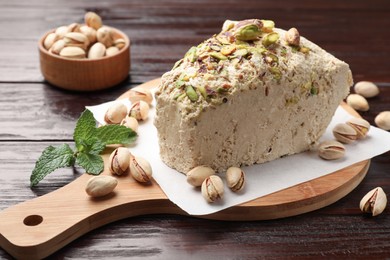 Photo of Piece of tasty halva with pistachios and mint on wooden table, closeup