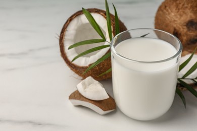 Photo of Glass of delicious vegan milk, coconut pieces and palm leaves on white marble table. Space for text
