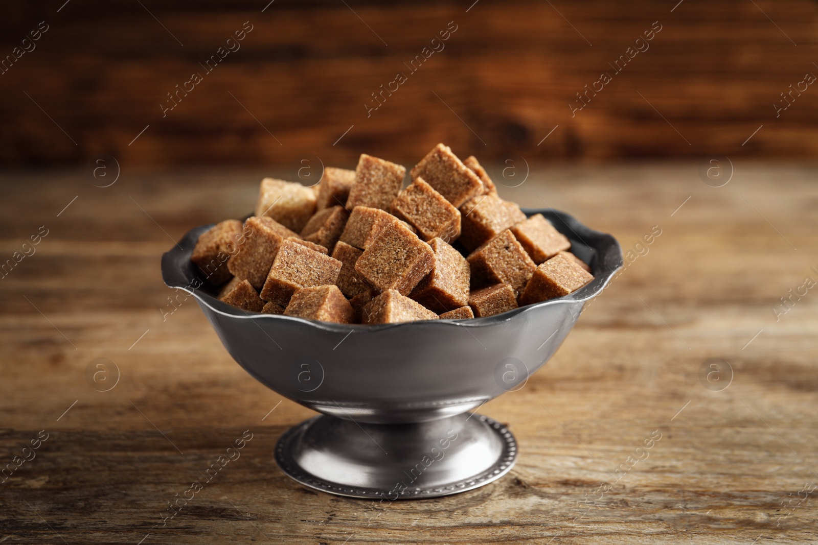 Photo of Brown sugar cubes in metal bowl on wooden table