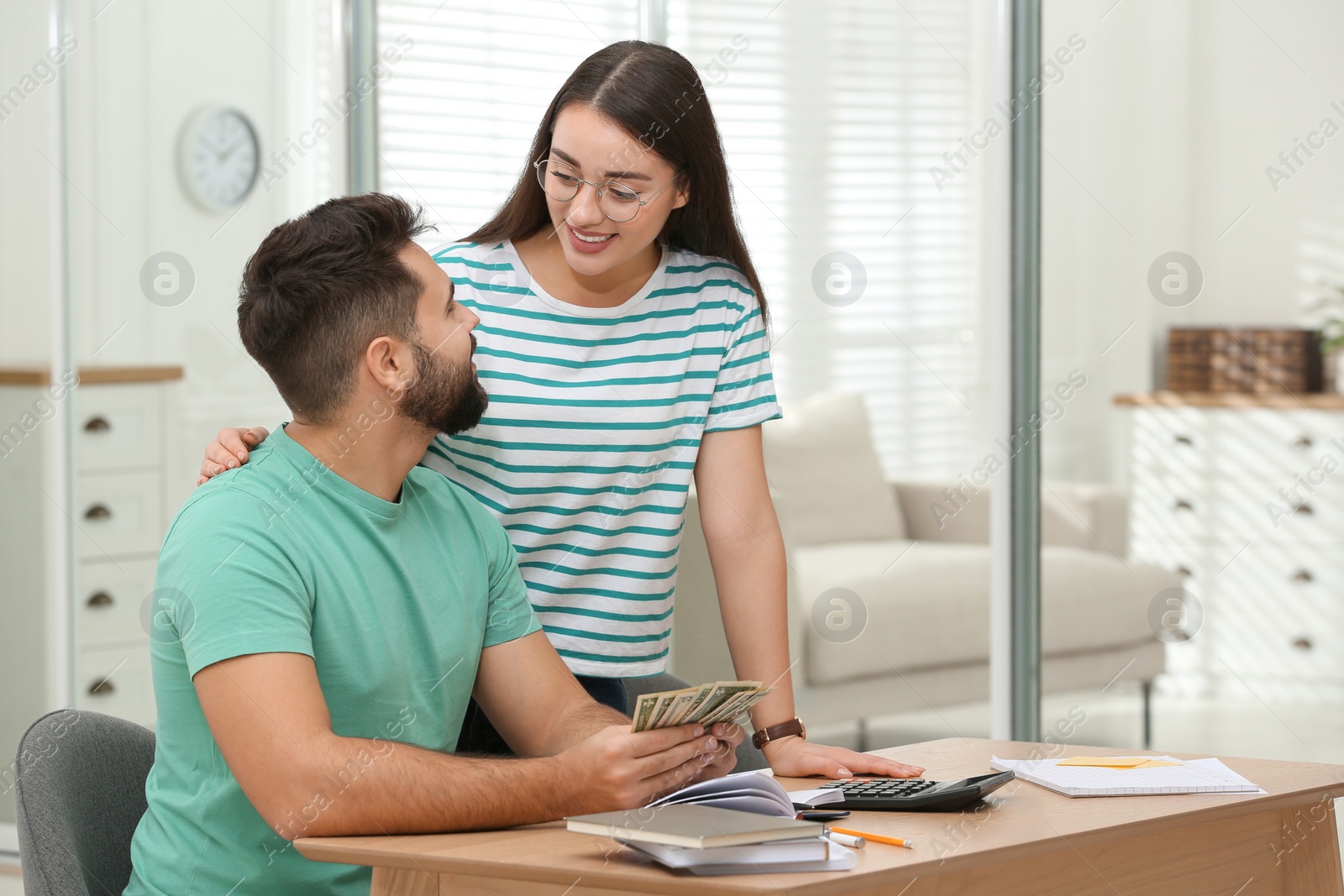 Photo of Happy young couple counting money at wooden table indoors