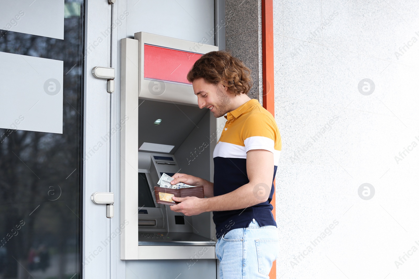 Photo of Young man with money near cash machine outdoors. Space for text