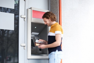 Young man with money near cash machine outdoors. Space for text