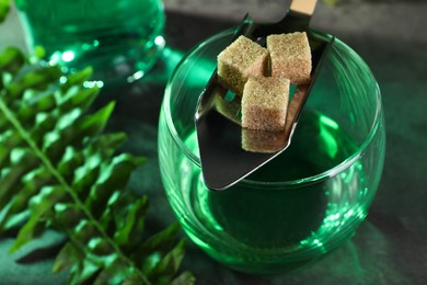 Photo of Absinthe in glass, spoon and brown sugar cubes on table, closeup. Alcoholic drink