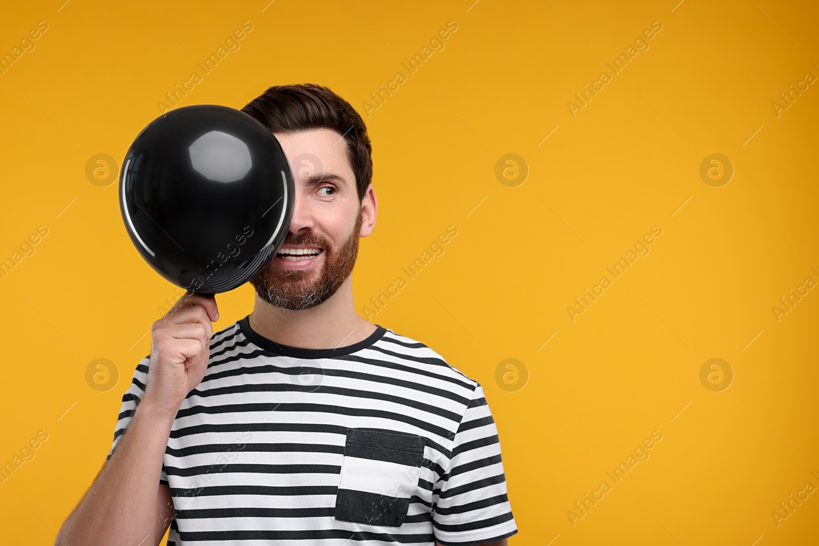 Photo of Happy man with black balloon on yellow background. Space for text