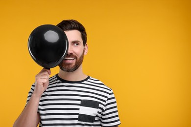 Happy man with black balloon on yellow background. Space for text