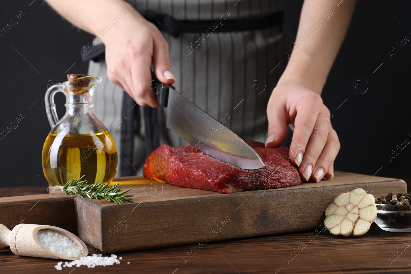 Photo of Woman cutting fresh raw beef steak at wooden table, closeup