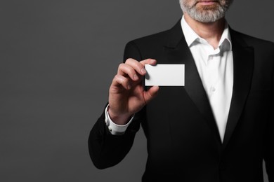 Man holding blank business card on grey background, closeup. Space for text