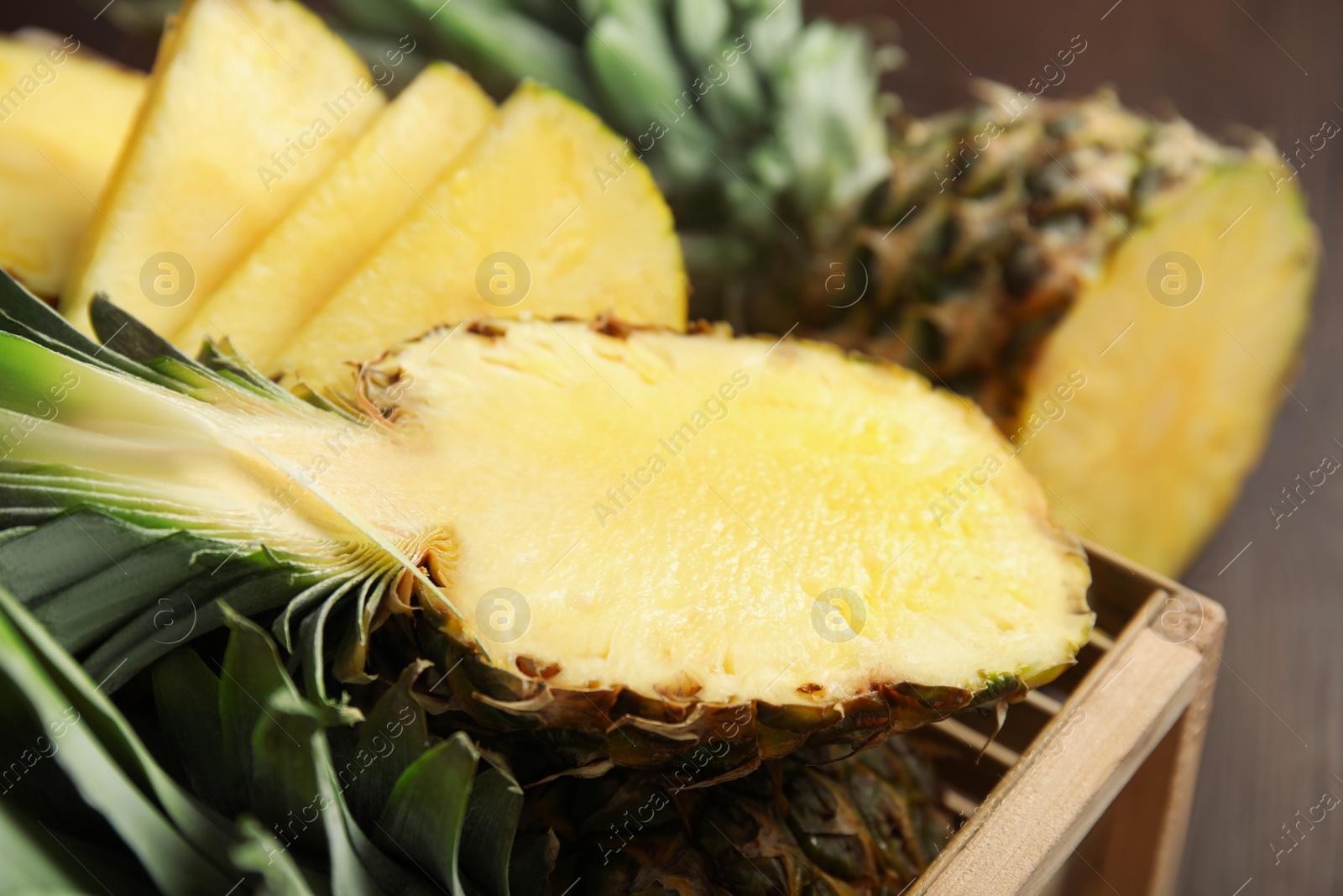 Photo of Tasty cut pineapples in wooden crate, closeup