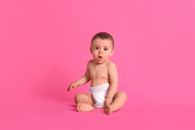 Cute baby in dry soft diaper sitting on pink background