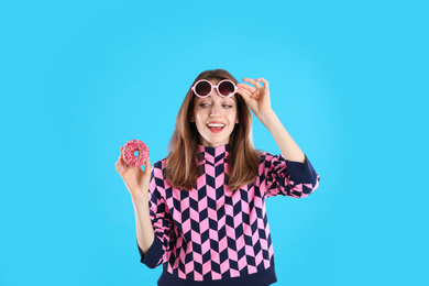 Photo of Beautiful young woman wearing sunglasses with donut on light blue background