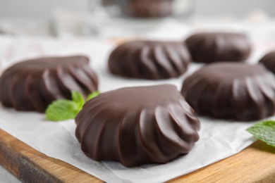 Photo of Delicious chocolate covered zephyrs and mint on wooden board, closeup