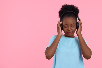 Young woman in headphones enjoying music on pink background. Space for text