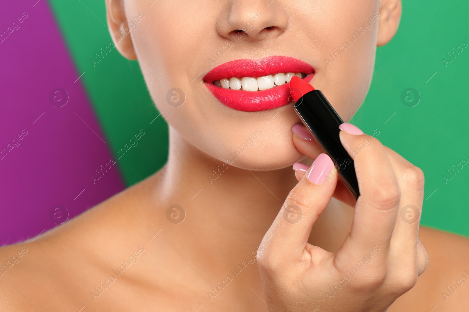 Photo of Young woman applying lipstick on color background, closeup