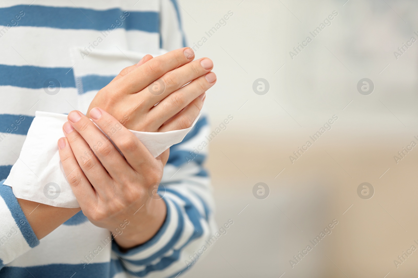 Photo of Woman cleaning hands with paper tissue on blurred background, closeup. Space for text