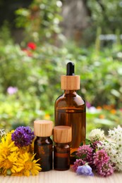 Photo of Bottles of essential oil and different flowers on white wooden table outdoors