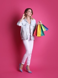 Beautiful young woman with shopping bags on color background