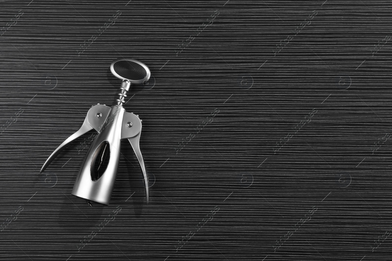 Photo of One wing corkscrew on black wooden table, top view. Space for text