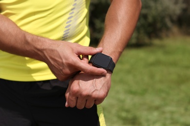 Photo of Young man checking pulse with smartwatch after training in park, closeup. Space for text
