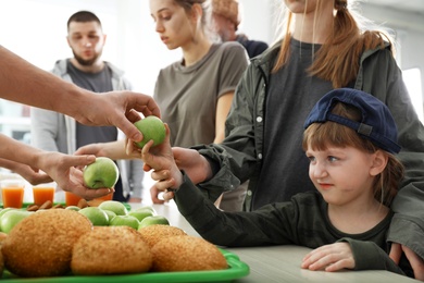 Volunteer giving apple to poor girl indoors
