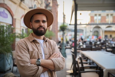 Photo of Portrait of handsome bearded man in hat on city street. Space for text